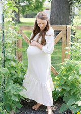 Pregnant woman in a cream Eliza Maternity and Nursing Dress, featuring cotton gauze, balloon sleeves, and a ruffle skirt.