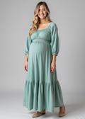 Smiling pregnant woman in a seafoam Eliza Maternity and Nursing Dress, featuring a smocked waist, balloon sleeves, and ruffle skirt in cotton gauze.