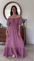 Woman in a mauve Ella maxi dress made of organic cotton gauze, featuring an off-shoulder scoop neck and smocked waist.