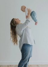 Woman in light blue oversized cotton/linen button-down shirt and jeans holding a baby.