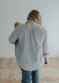 Woman from behind wearing an oversized blue pinstripe cotton/linen button-down shirt, holding a baby.