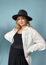 Blonde pregnant woman in a white oversized cotton/linen button-down shirt, black tank, black skirt, and black hat.