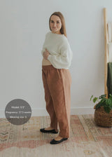 Pregnant woman in rust linen/cotton barrel pants with a stretchy waistband and deep pockets.