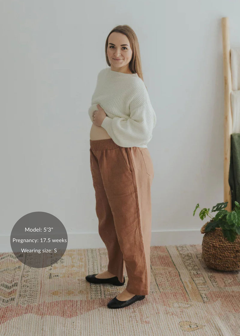 Pregnant woman in rust linen/cotton barrel pants with a stretchy waistband and deep pockets.