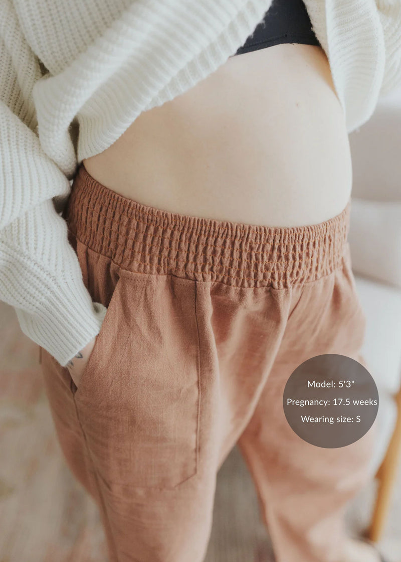 Close-up of a pregnant belly wearing rust-colored linen/cotton barrel pants with an elastic waistband and deep pockets.