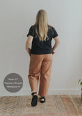 Woman from behind in rust linen/cotton barrel pants with a black tee and sandals.