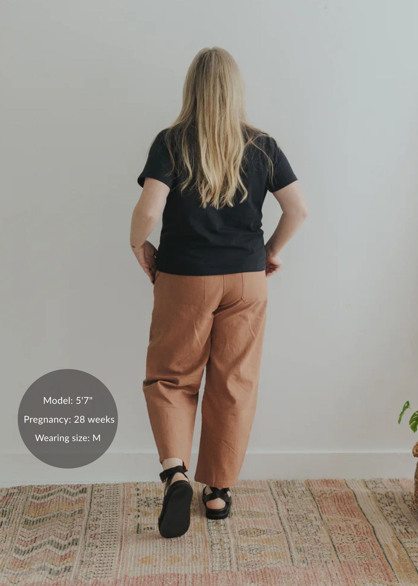 Woman from behind in rust linen/cotton barrel pants with a black tee and sandals.