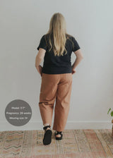 Woman from behind in rust linen/cotton barrel pants with a black tee and sandals.