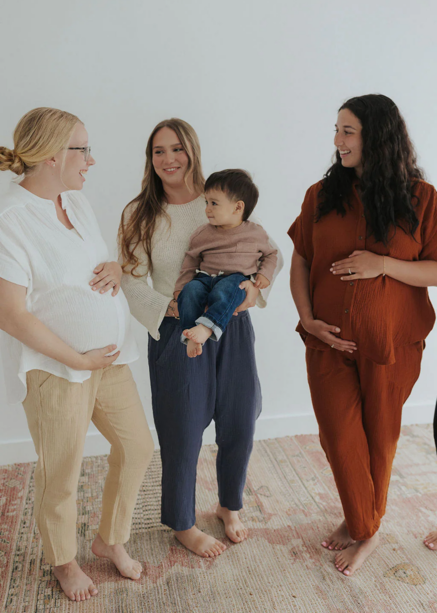 Three women, two pregnant, and one holding a baby, wearing Everyday Breeze Pants in cotton gauze.