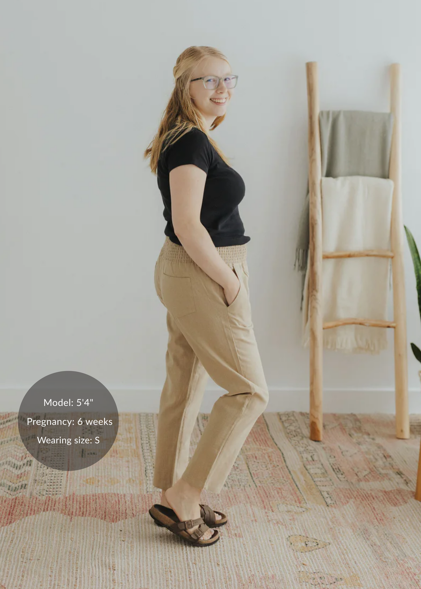 Blonde model wearing tan smocked linen maternity pants with pockets and a black t-shirt.
