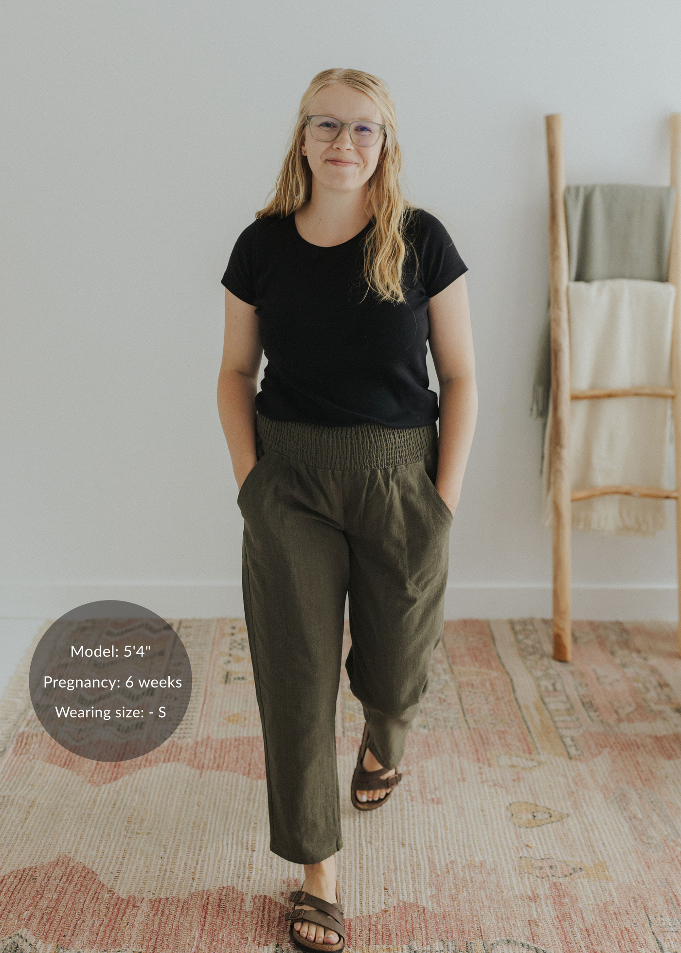 Blonde model wearing olive green smocked linen maternity pants with pockets and a black t-shirt.