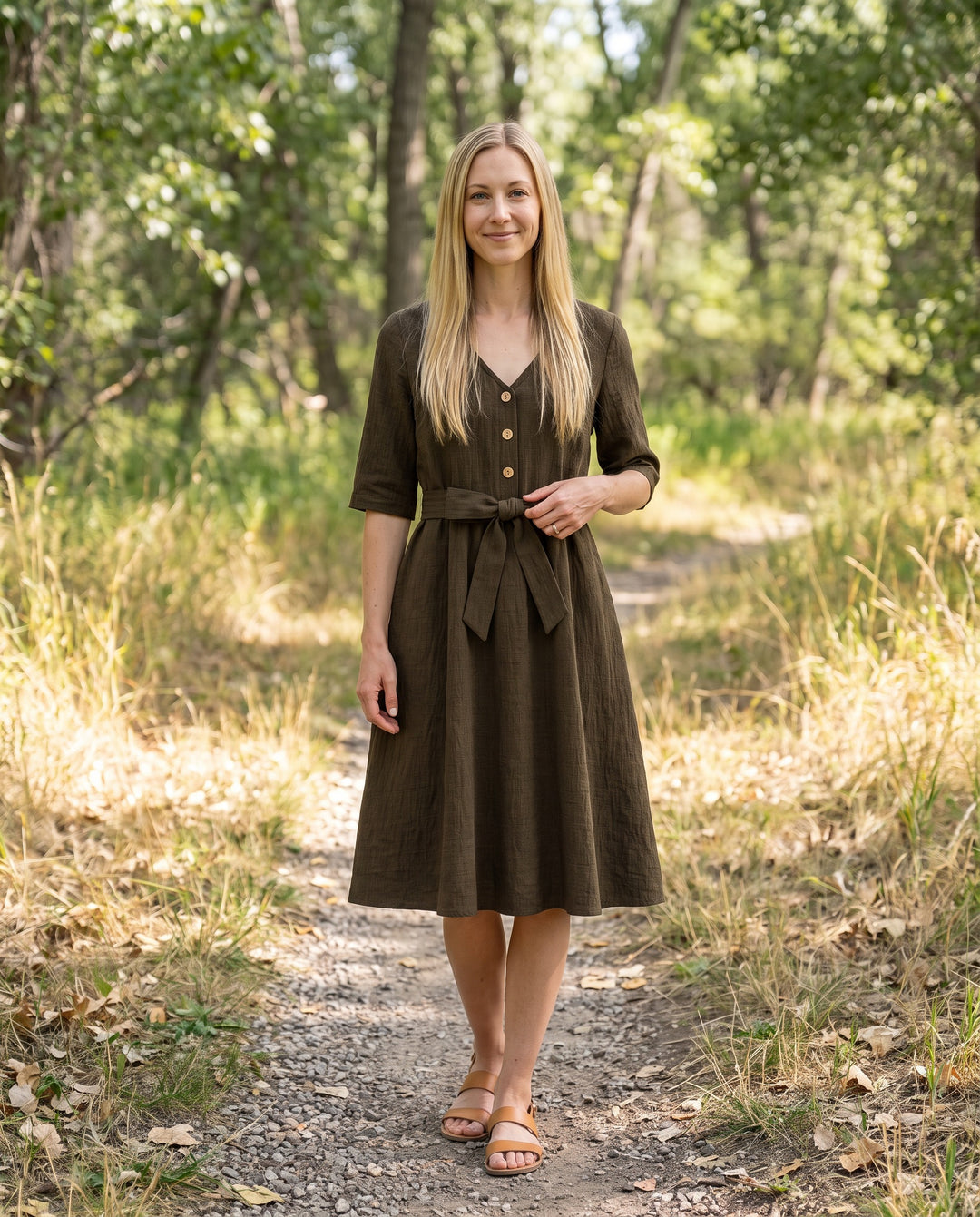 Woman wearing the Faye Dress in Olive sandwashed linen on a wooded trail