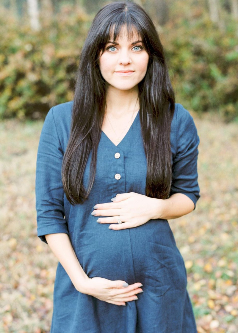 Pregnant woman in a navy blue linen Faye Dress with a V-neck, front buttons, and a-line silhouette.