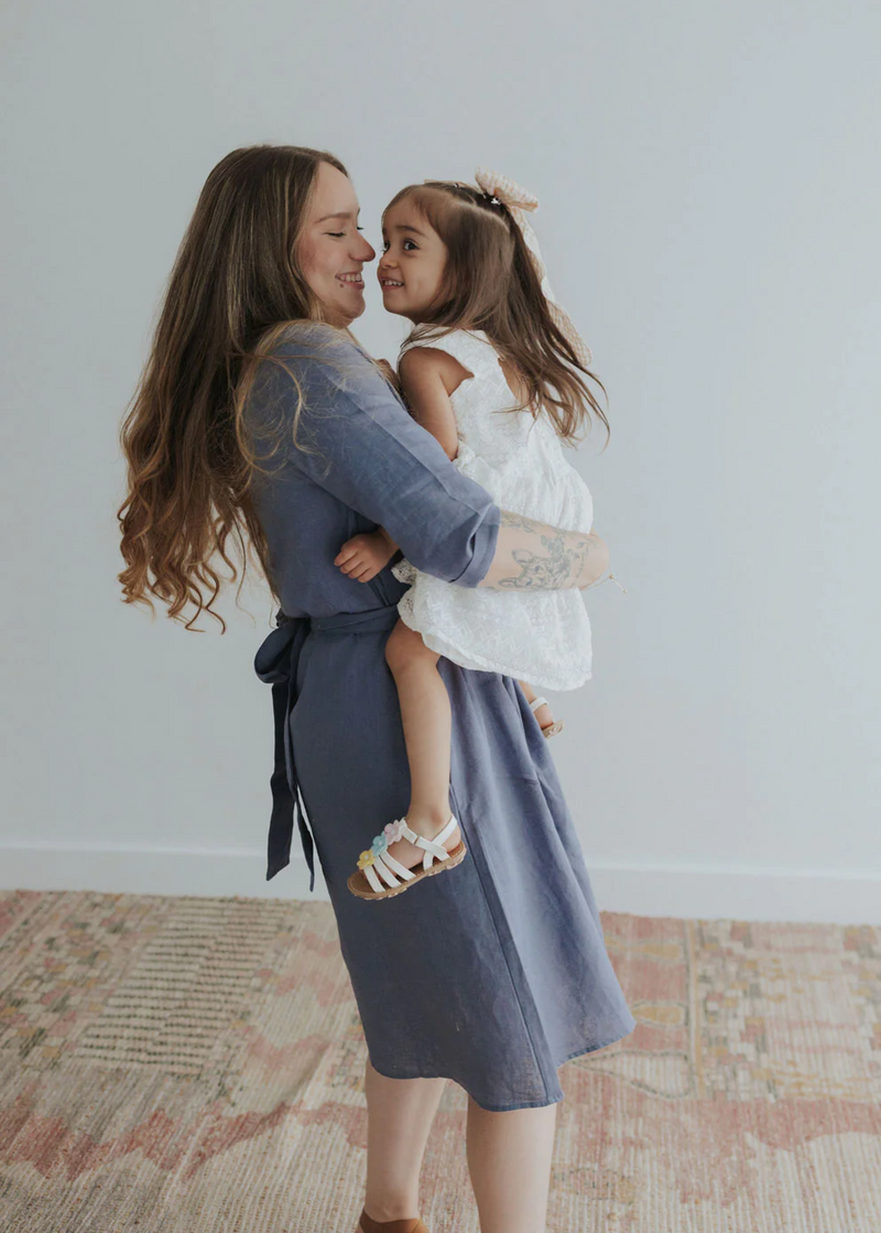 Woman in a blue linen Faye Dress with front buttons and waist tie, holding a child.