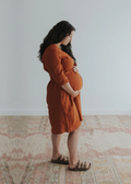 Pregnant woman in a rust linen Faye Dress with front buttons, v-neck, and side pockets.