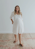 Smiling woman in a white linen Faye Dress with front buttons, v-neck, and pockets.