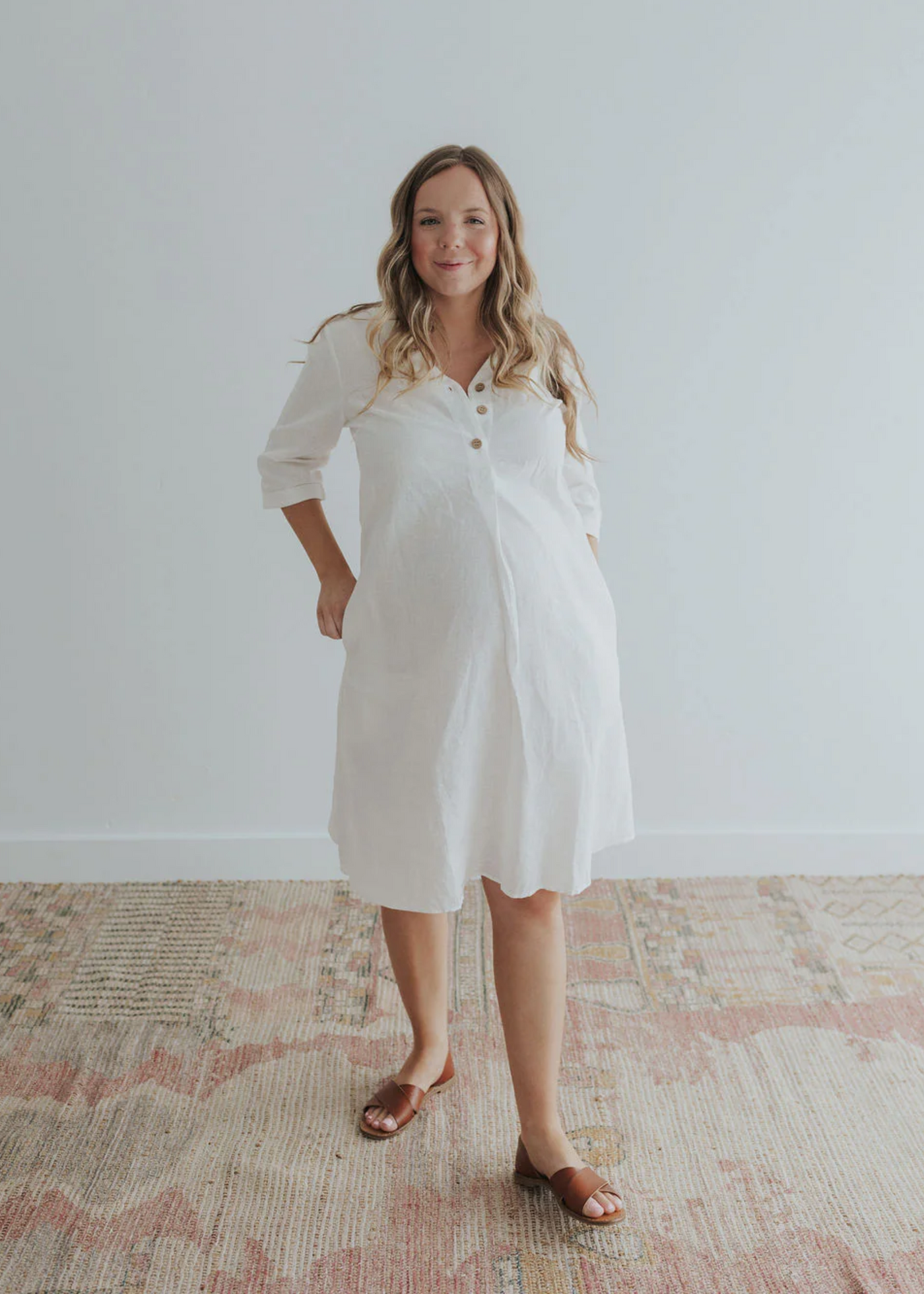 Smiling woman in a white linen Faye Dress with front buttons, v-neck, and pockets.