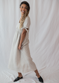 Smiling woman in a natural linen-cotton Florence Midi Dress with tied sleeves and relaxed silhouette.