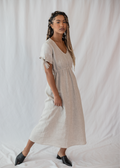 Woman in a natural linen-cotton Florence Midi Dress with V-neck, elastic waist, and bow-tie sleeves.
