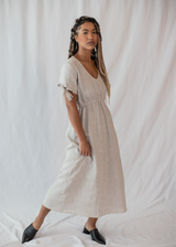 Woman in a natural linen-cotton Florence Midi Dress with V-neck, elastic waist, and bow-tie sleeves.