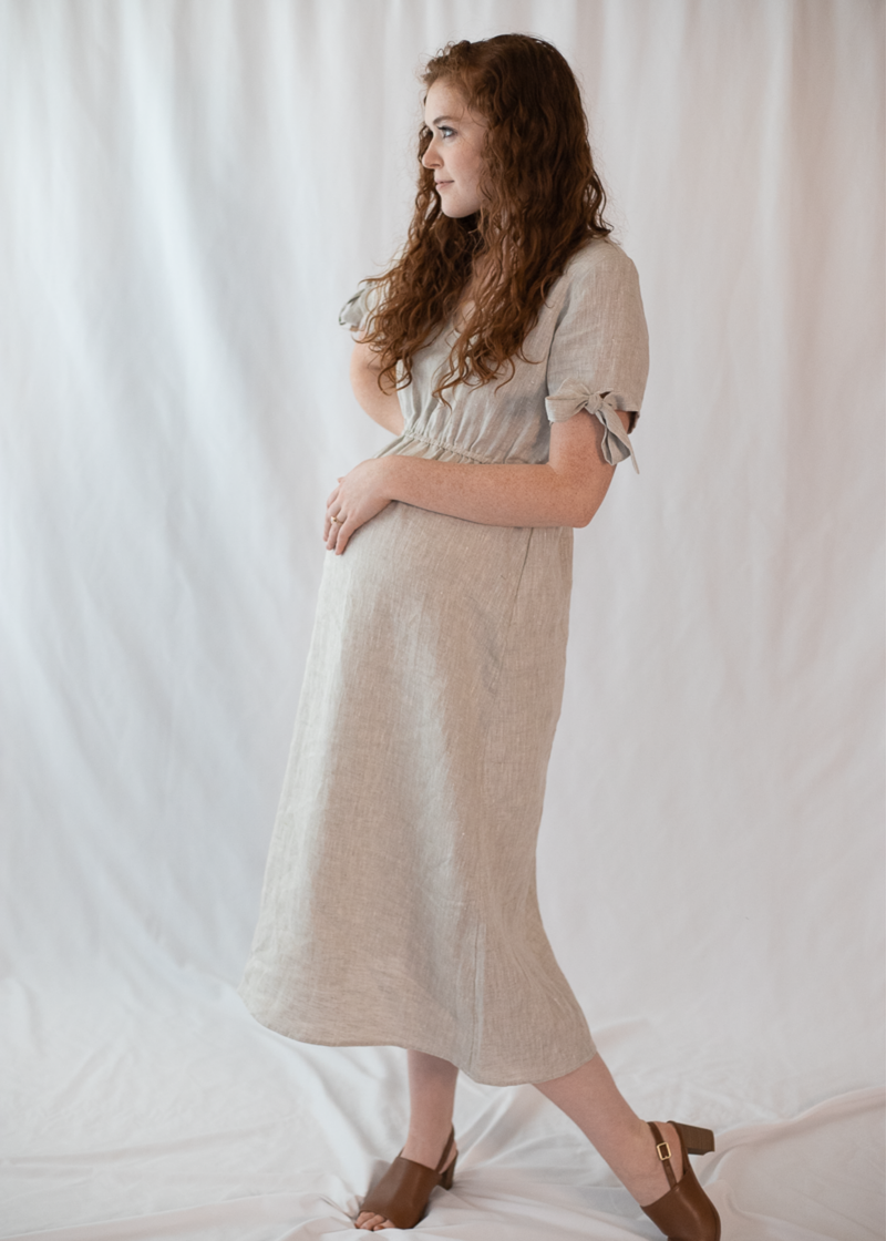 Pregnant woman in a natural linen-cotton Florence Midi Dress with ruched waist and tie sleeves.