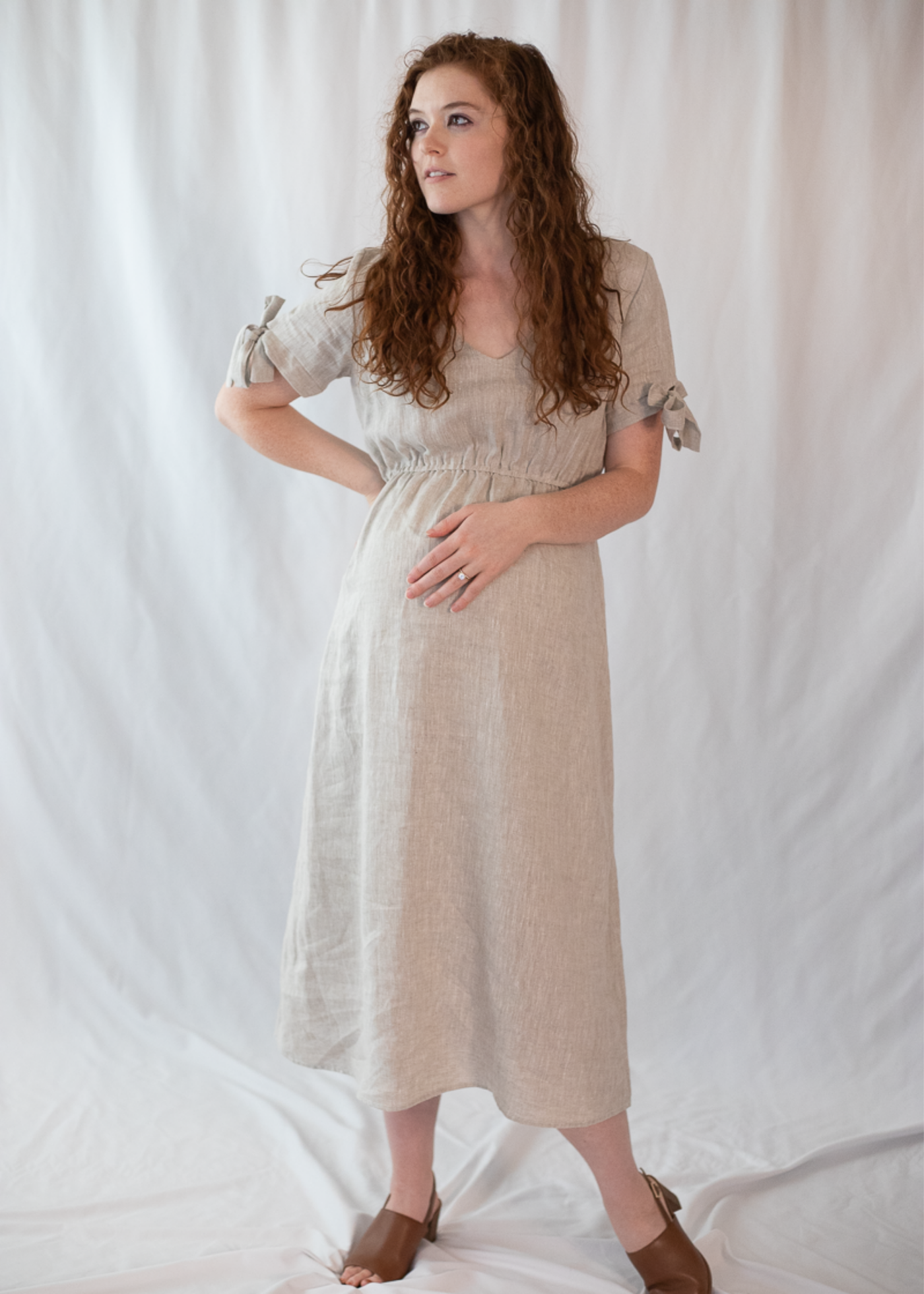 Pregnant woman in a natural linen-cotton Florence Midi Dress with tied sleeves and a relaxed silhouette.