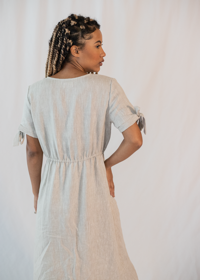 Woman in a light grey linen-cotton Florence Midi Dress with tied sleeves and an elasticated waist, viewed from the back.