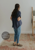 Woman in a loose navy cotton gauze button-down top and light blue pants, seen from behind.