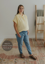 Pregnant woman in a light yellow cotton gauze button-down top and blue pants.