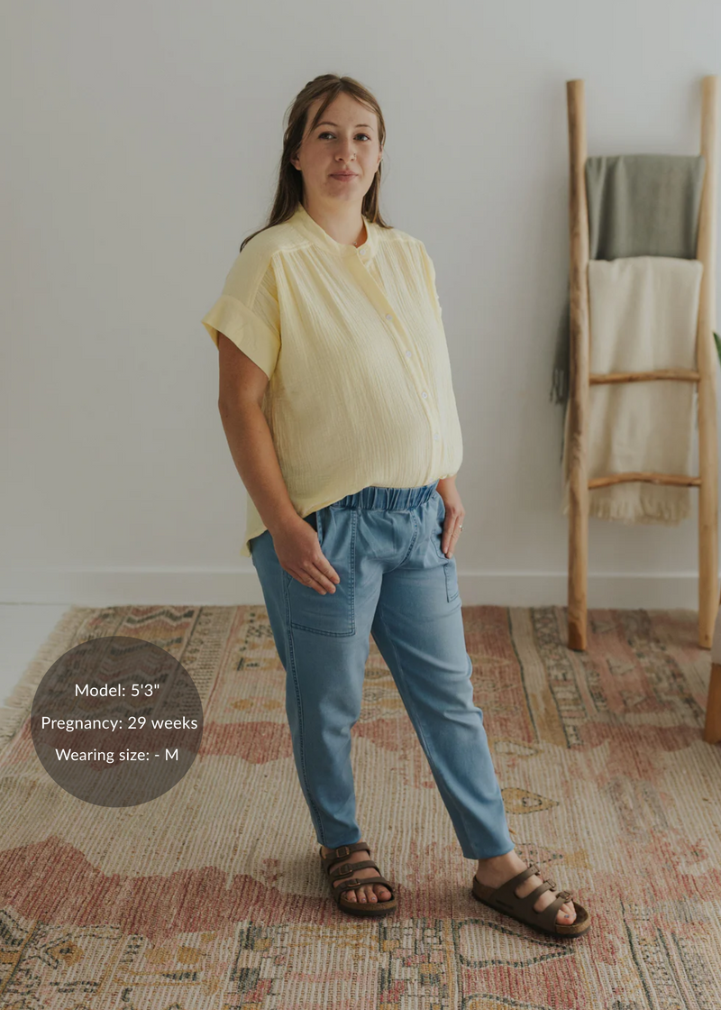 Pregnant woman in a light yellow cotton gauze button-down top and blue pants.