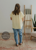 Woman from behind wearing an oversized light yellow cotton gauze button-down top and blue pants.