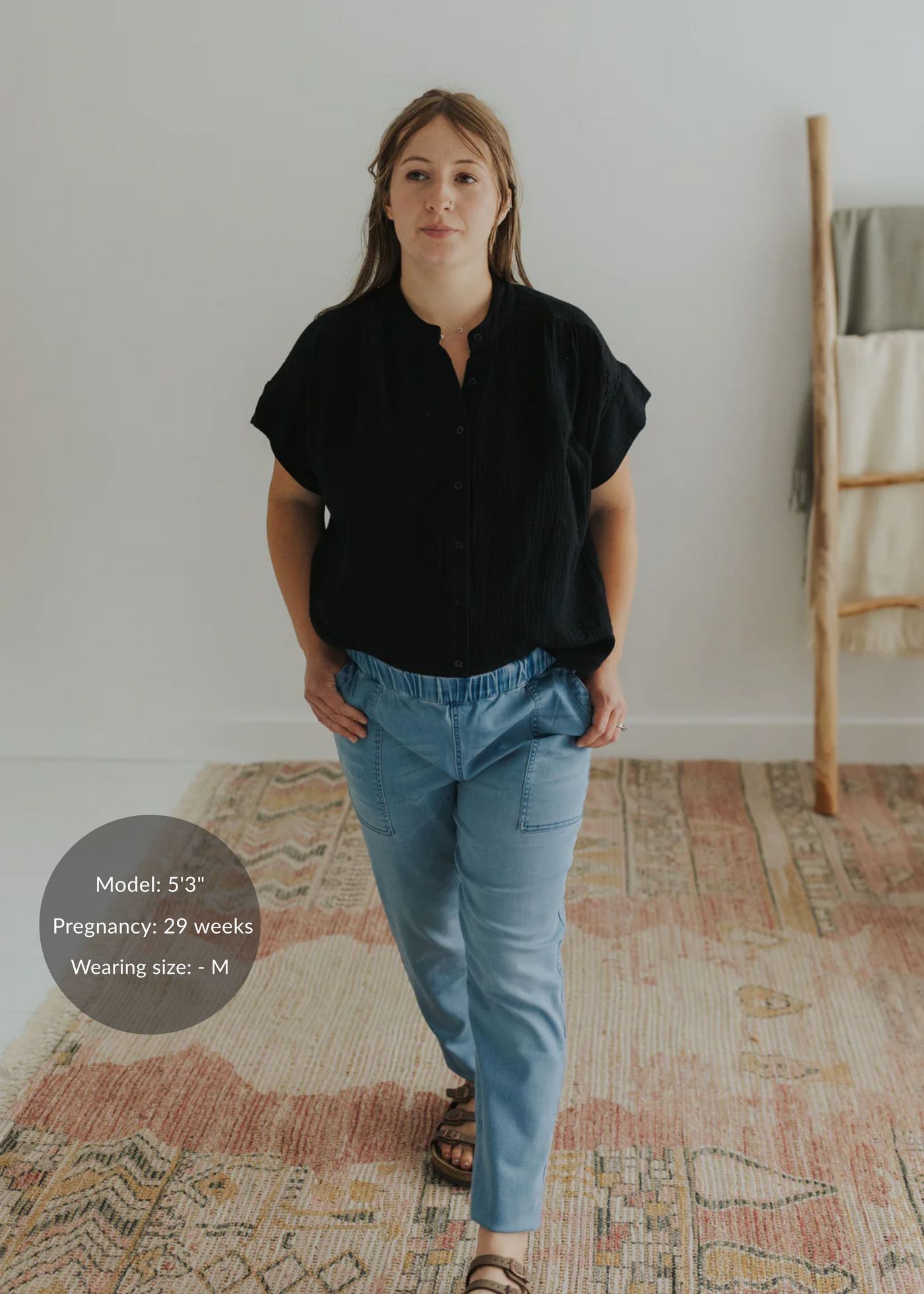 Woman in black cotton gauze button-down top and light blue pants, hands in pockets.