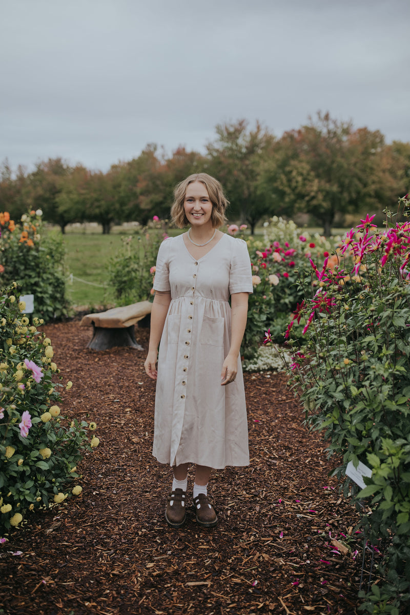 Woman in the Beige Hazel Front Button Dress, front view, midi length in a dahlia garden