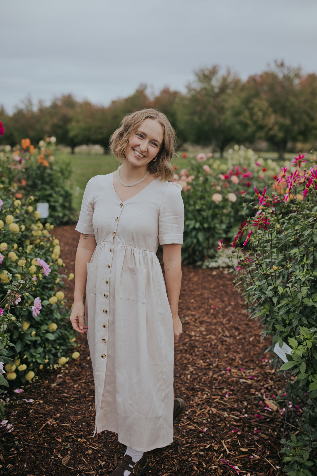 Smiling woman in the Beige Hazel Front Button Dress, front view showing the buttons and short sleeves
