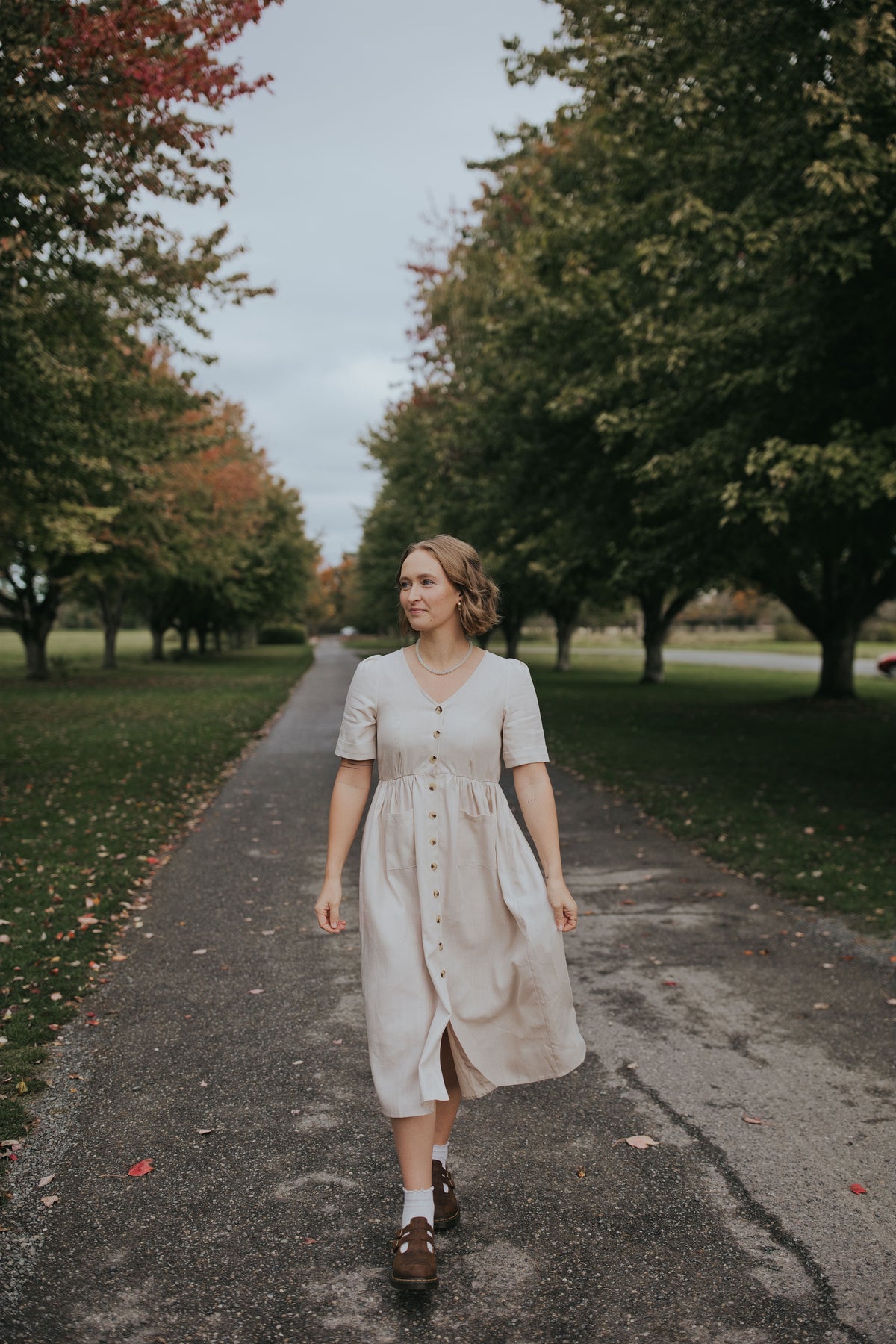 Woman walking in the Beige Hazel Front Button Dress on a tree-lined path