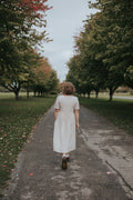 Back view of the Beige Hazel Front Button Dress on a tree-lined path