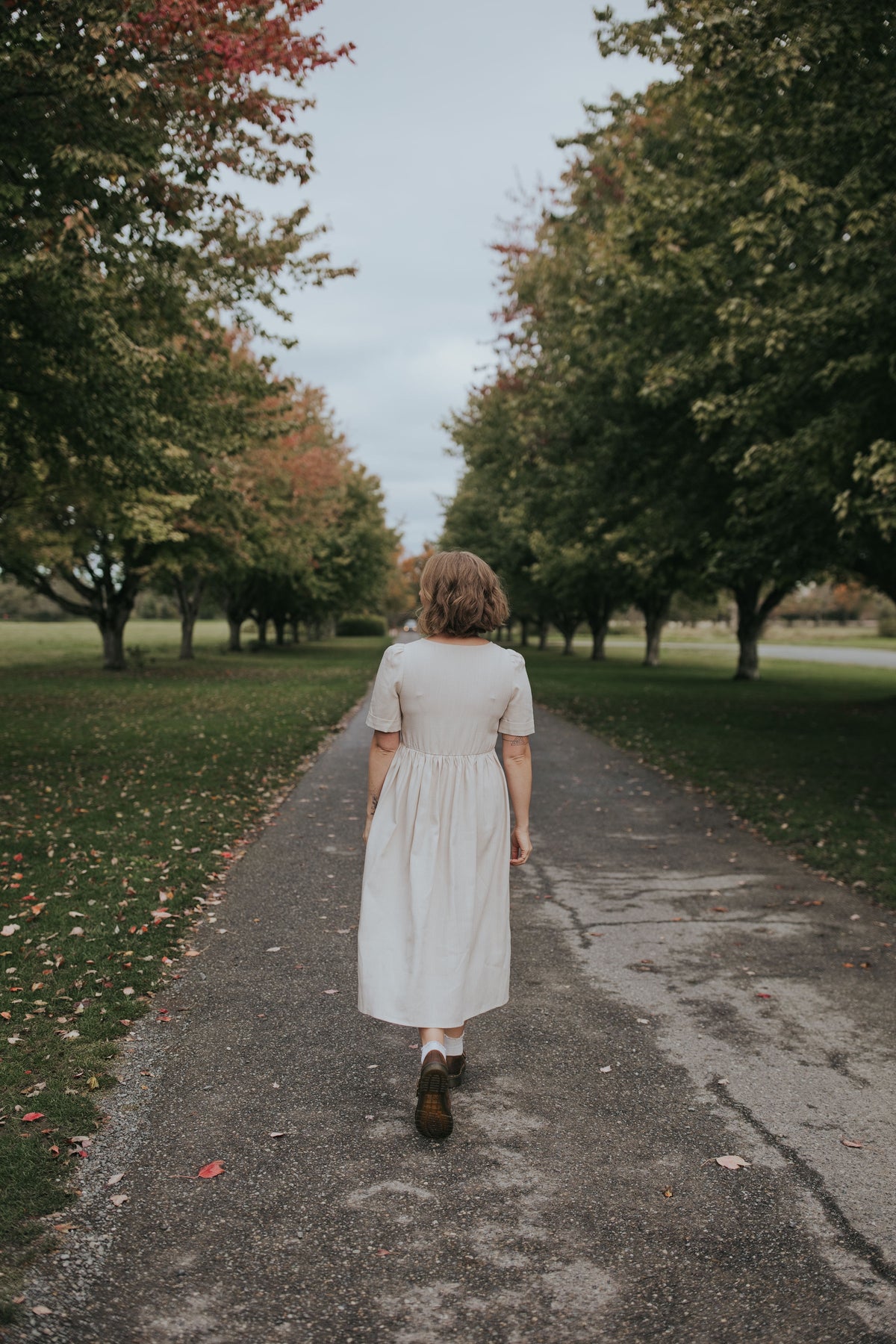Back view of the Beige Hazel Front Button Dress on a tree-lined path