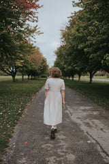 Back view of the Beige Hazel Front Button Dress on a tree-lined path