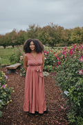 Woman in the Dusty Rose Iris Sleeveless Wrap Dress, front view, full length in a dahlia garden