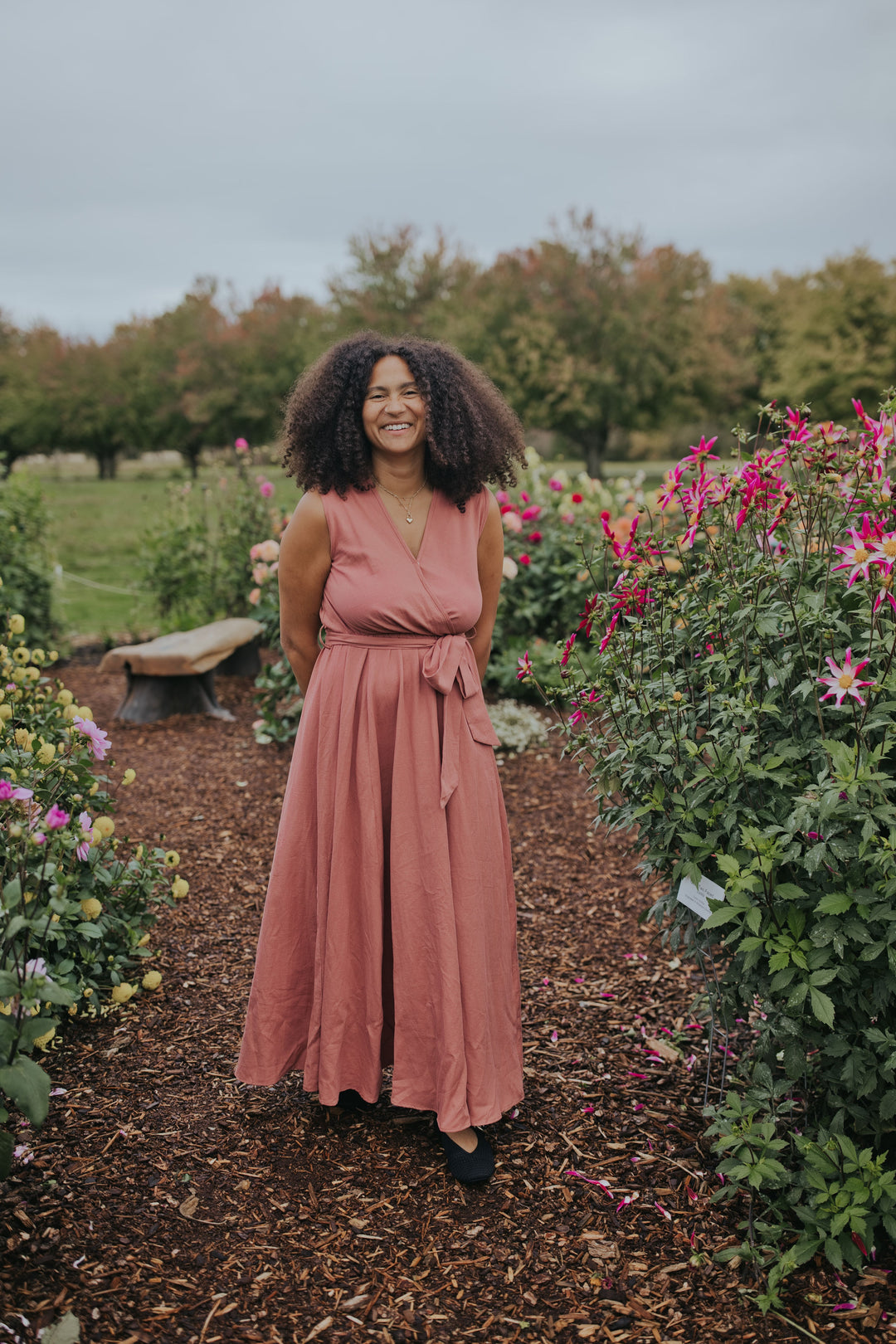 Smiling woman in the Dusty Rose Iris Sleeveless Wrap Dress, front view showing the V-neck and waist tie