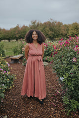 Smiling woman in the Dusty Rose Iris Sleeveless Wrap Dress, front view showing the V-neck and waist tie