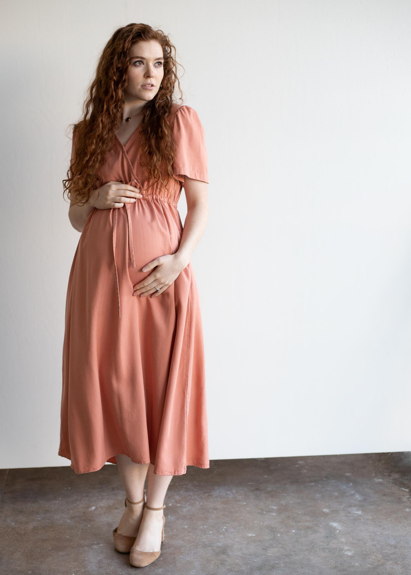 Pregnant woman in a peach lyocell Jasmine Dress with short sleeves, holding her belly.