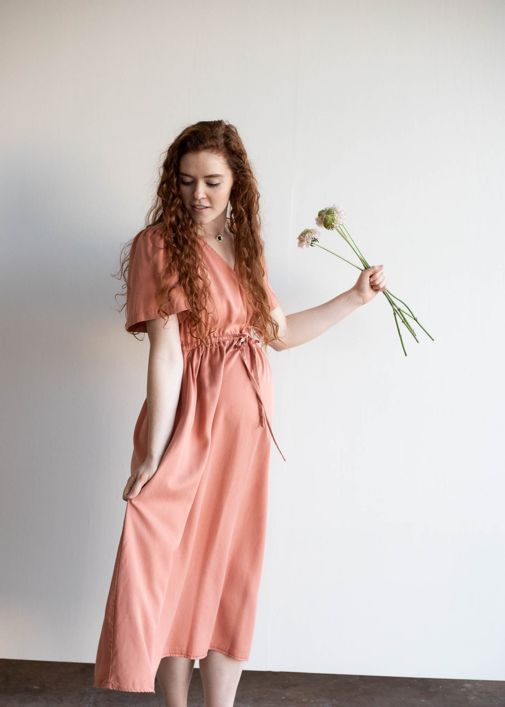 Pregnant woman in a peach lyocell Jasmine Dress with short sleeves, holding flowers.