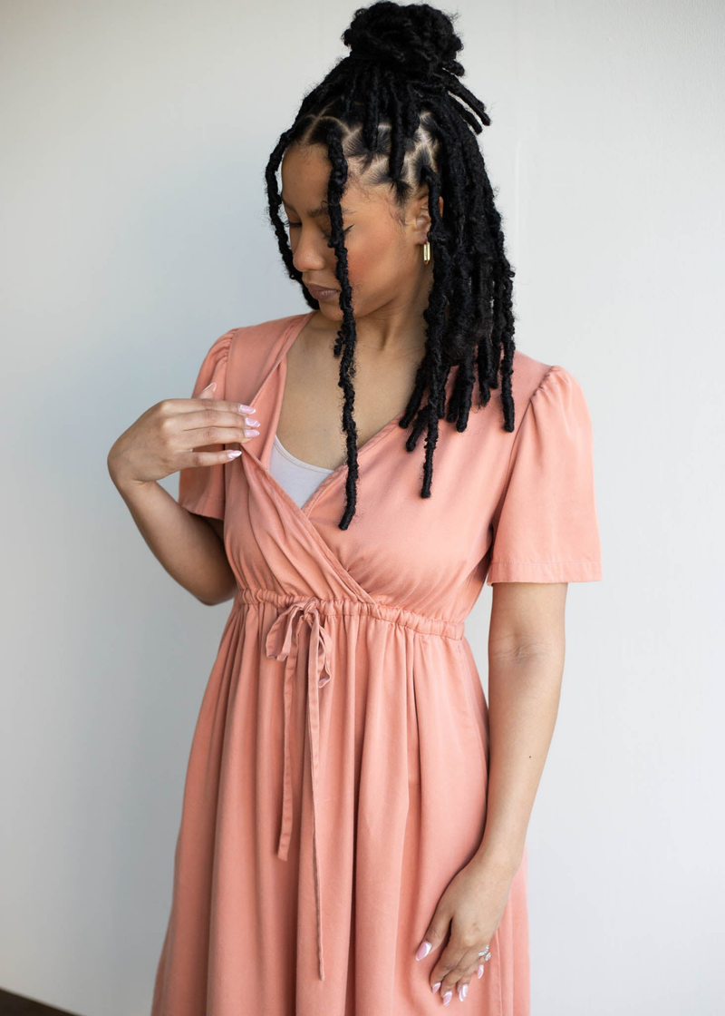 Woman in a peach lyocell Jasmine Dress with a relaxed silhouette, showing discreet nursing access.