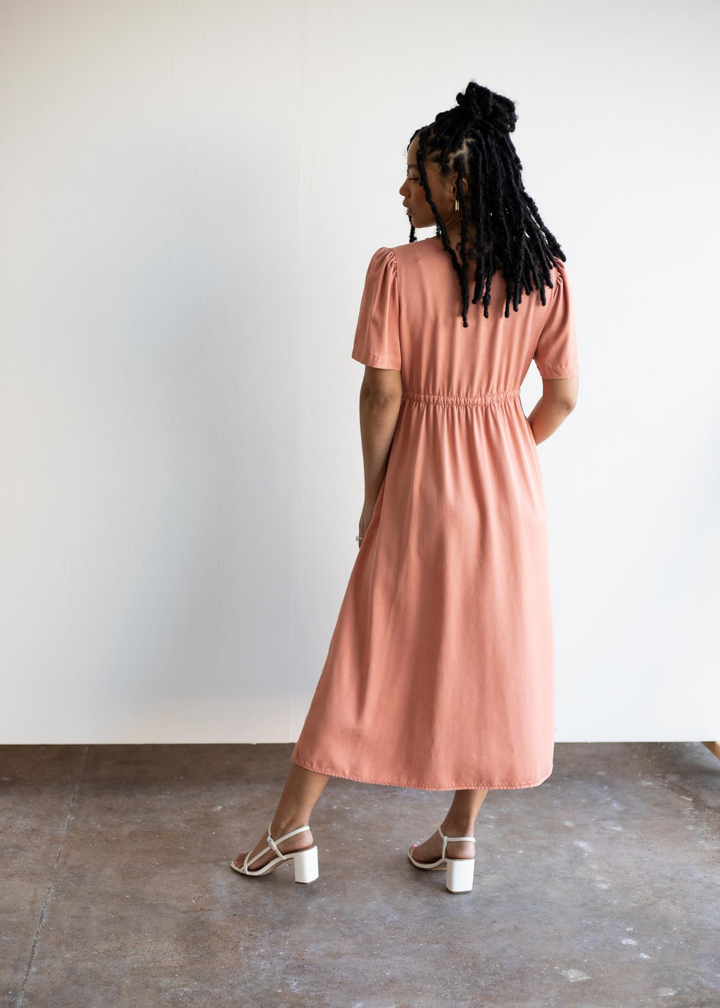 Woman from behind wearing a peach lyocell Jasmine Dress with short puff sleeves and an elastic waist.