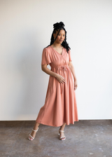 Woman in a peach lyocell Jasmine Dress with V-neck, short sleeves, and drawstring waist.