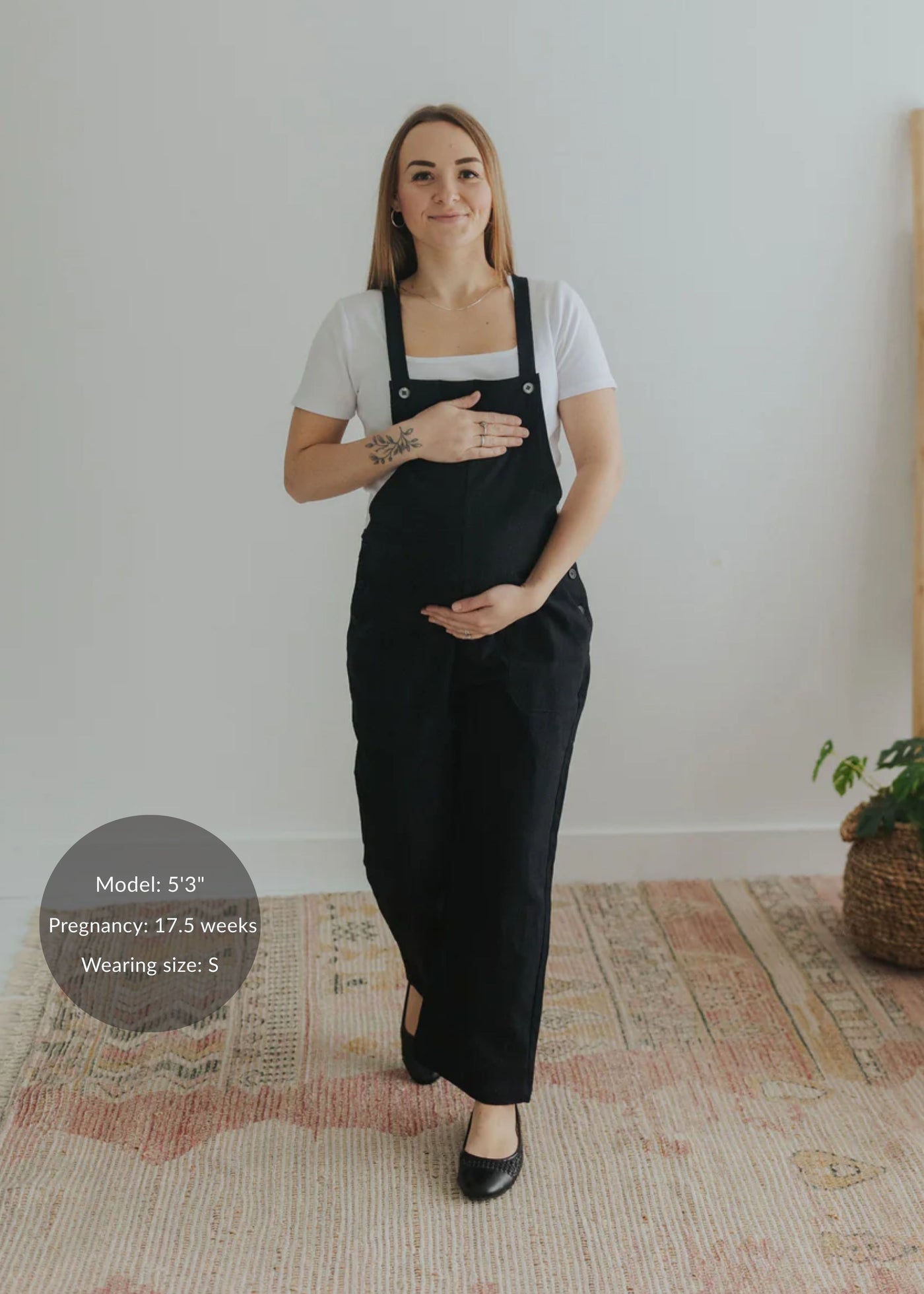 Smiling pregnant woman in black linen/cotton Journey Overalls with adjustable straps and deep pockets.
