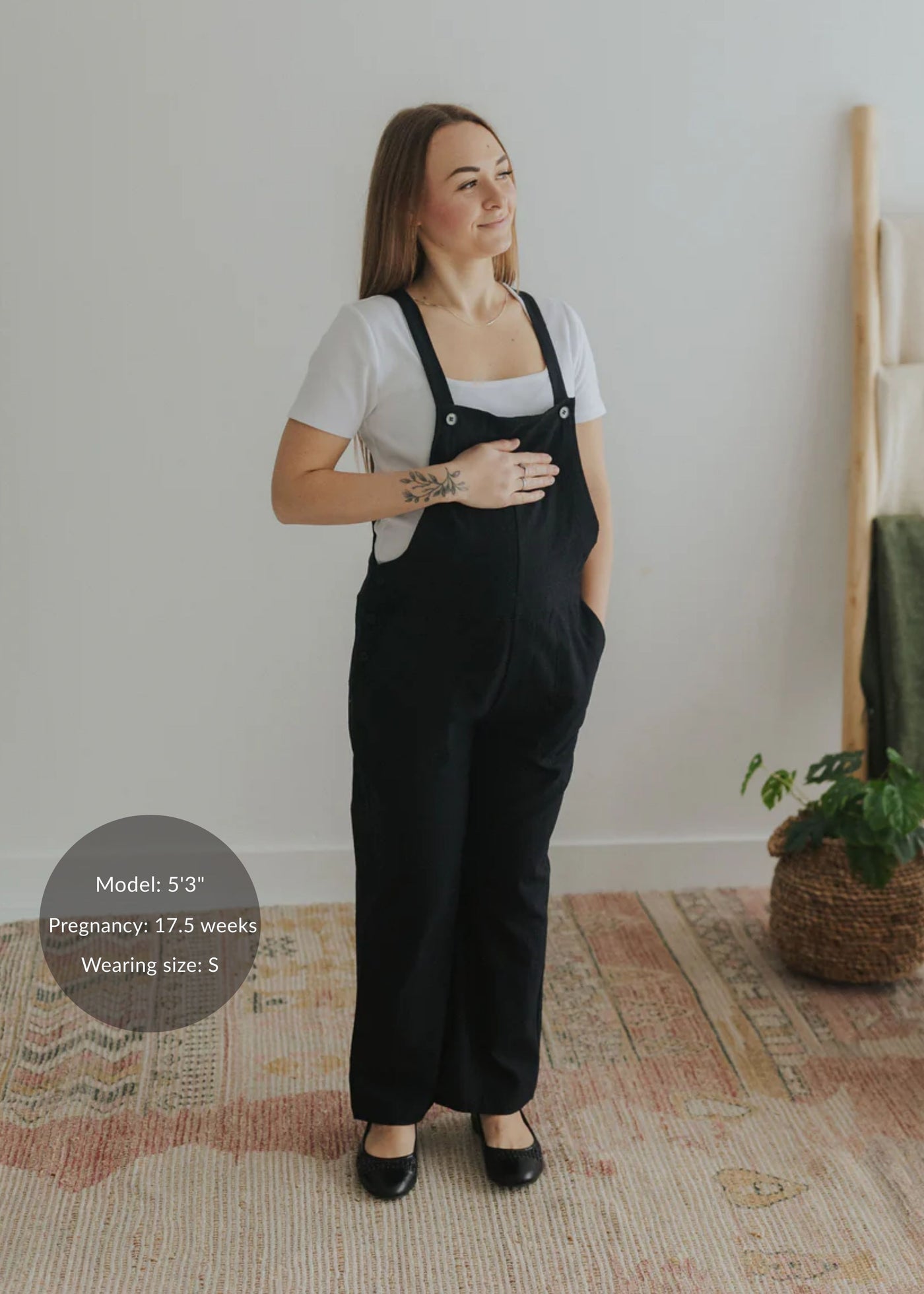 Pregnant woman in black linen/cotton Journey Overalls with adjustable straps, deep pockets, and side buttons.