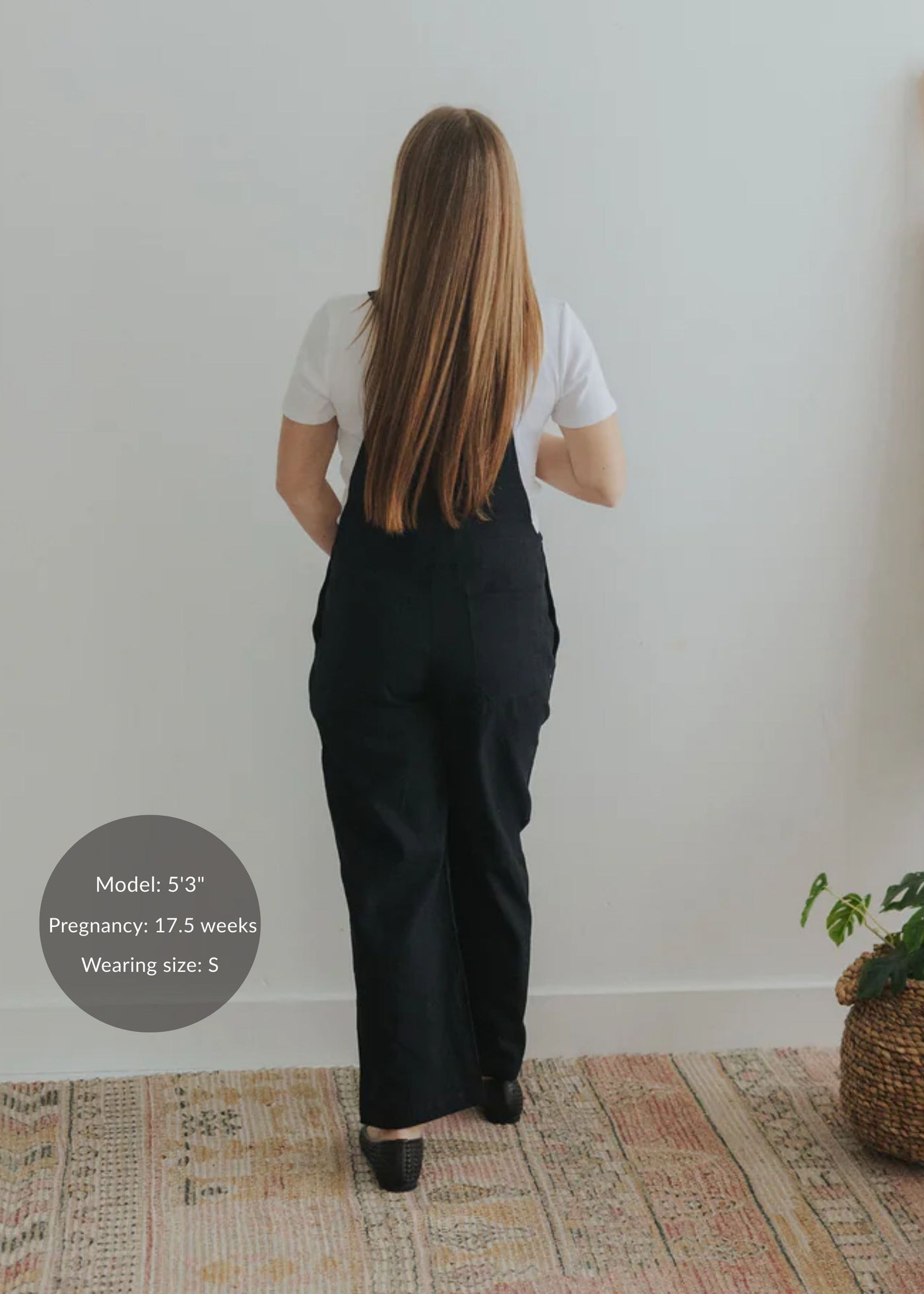 Back view of a pregnant model wearing black linen/cotton Journey Overalls in size S over a white tee.