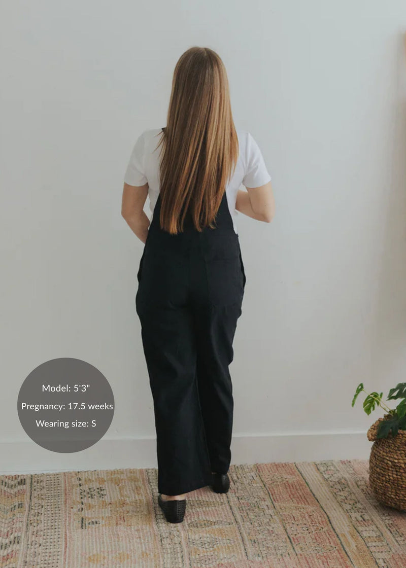 Back view of a pregnant model wearing black linen/cotton Journey Overalls in size S over a white tee.